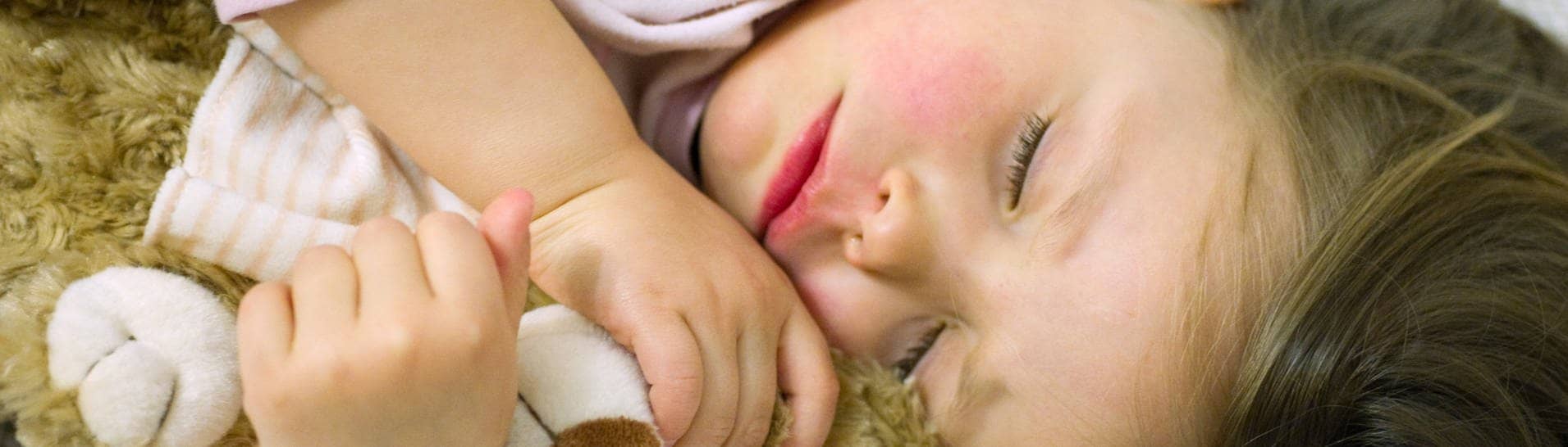 Notaufnahme soll Gebühren kosten? Ein kleines Mädchen mit roten Wangen schläft mit ihrem Teddy im Arm.