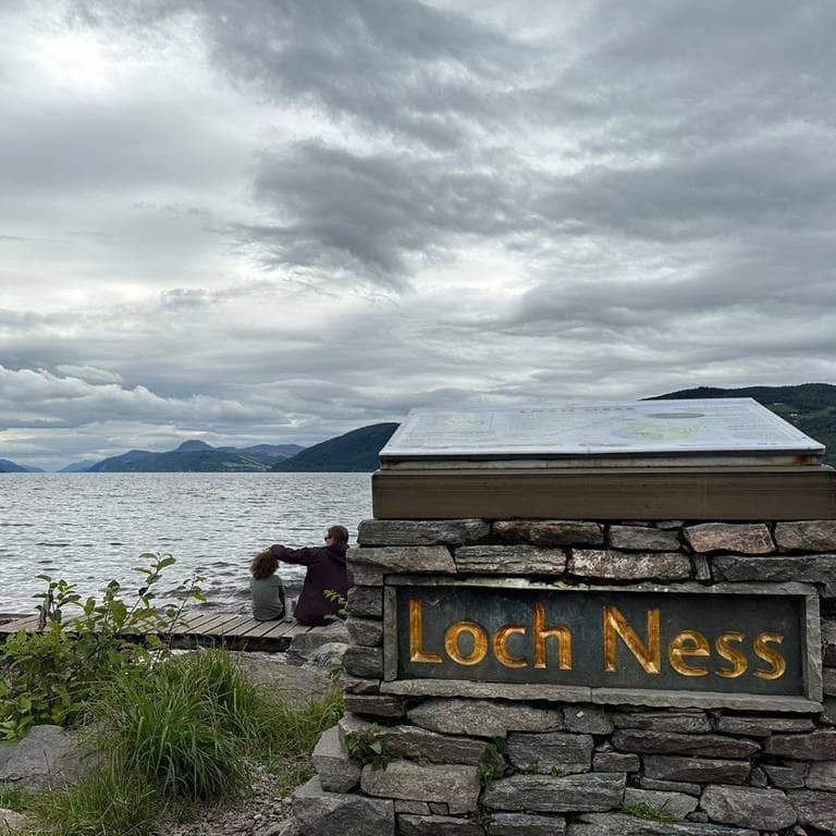 Menschen sitzen am Ufer des Loch Ness in Schottland.