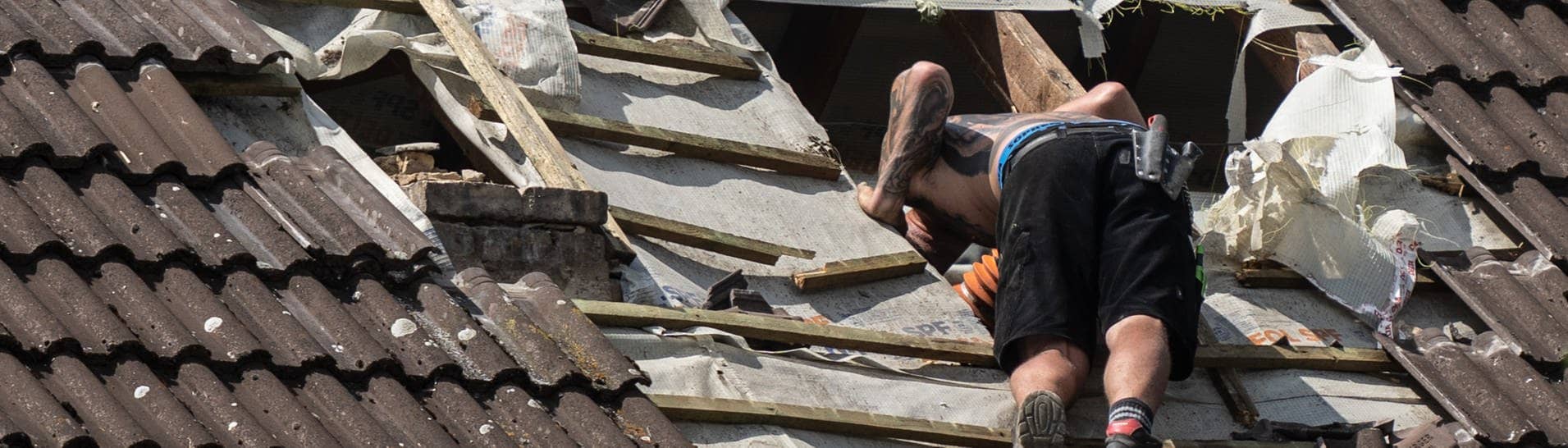 Dachdeckermeisterin verteidigt Azubi gegenüber Kundin. Auf dem Bild ist zu sehen: Ein Mitarbeiter eines Dachdeckerunternehmens schaut in ein großes Loch in einerm Dach. (Symbolbild)