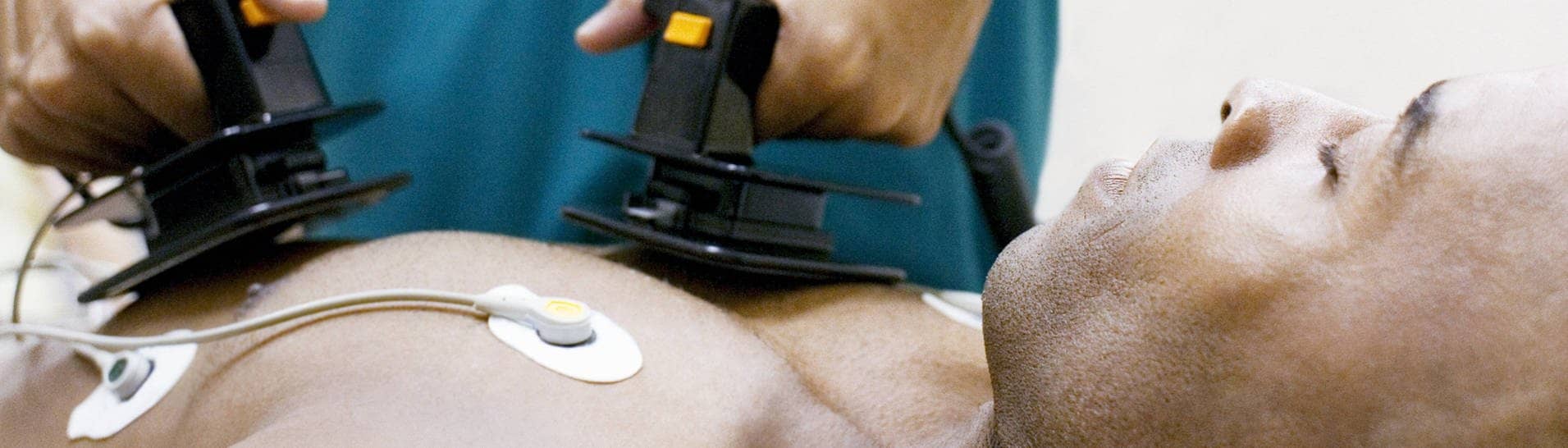 Ein bewusstloser Mann liegt, während ein Mediziner ihm einen Defibrillator auf die Brust hält