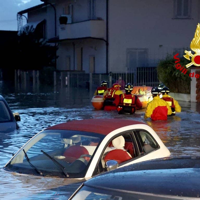Feuerwehrleute schieben ein Schlauchboot durch eine überschwemmte Straße, in der zahlreiche Autos unter Wasser stehen