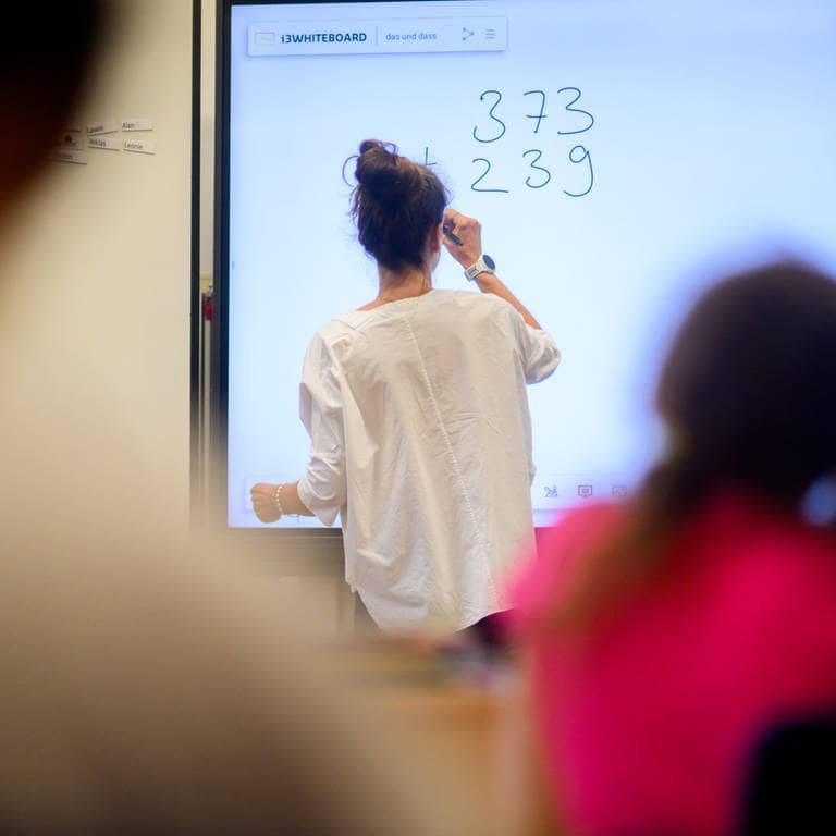 Eine Lehrerin schreibt eine Mathematikaufgabe auf eine digitale Schultafel im Klassenraum einer 4. Klasse einer Grundschule. (Foto: dpa Bildfunk, picture alliance/dpa | Julian Stratenschulte)