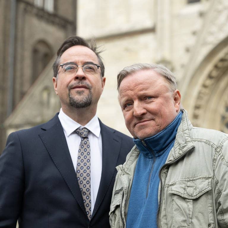 Tatort Münster: Die Schauspieler Jan Josef Liefers (l. Prof. Karl-Friedrich Boerne) und Axel Prahl (als Kommissar Thiel) stehen bei einem Fototermin vor der Liebfrauen-Überwasserkirche.