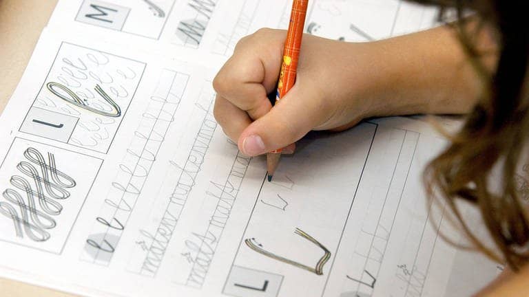 Ein Grundschulkind übt, ein L zu schreiben (Foto: IMAGO, imago/Marco Stepniak)