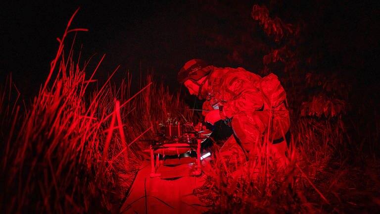 Ein ukrainischer Soldat in der Region Charkiw schaltet eine Selbstmord-FPV-Drohne in der Startposition ein. Das Bild ist durch die Nachtsichtaufnahme rot gefärbt.