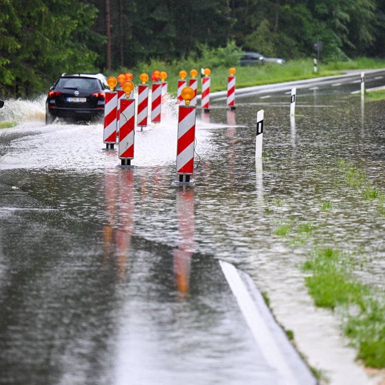 Autos fahren durch eine von Hochwasser betroffene Kreisstraße zwischen Beuren und Illerrieden.