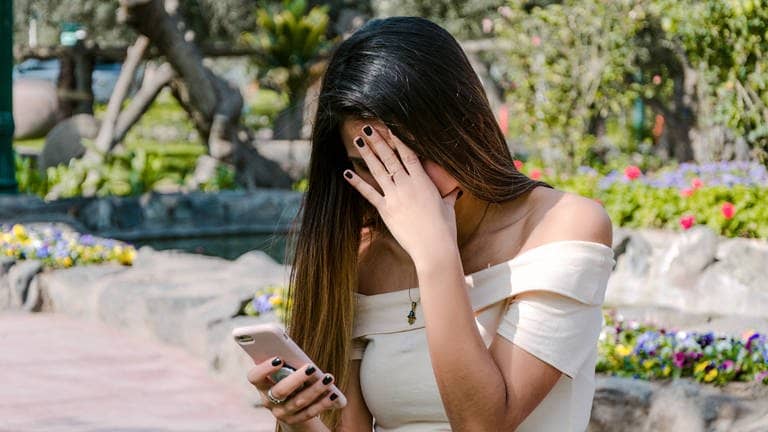 Ein Mädchen schaut auf ihr Smartphone und verdeckt mit ihrer Hand ihr Gesicht.