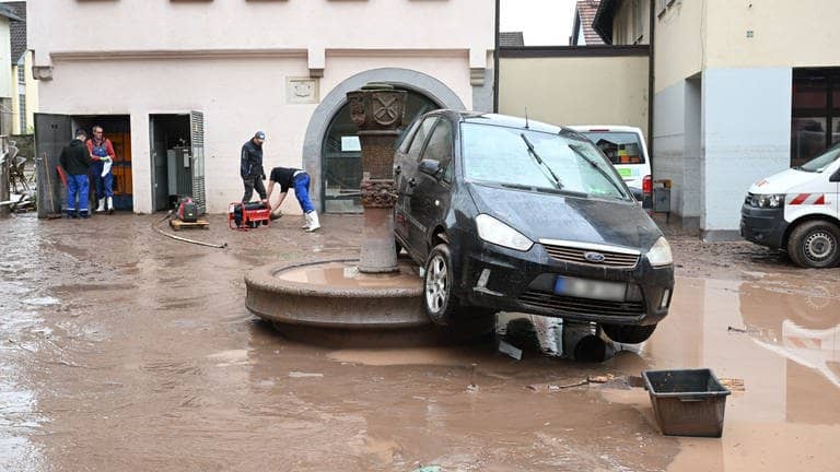 Auf einem Brunnen in Rudersberg steht ein durch ein Hochwasser weggespültes Auto. Seit Tagen kämpfen die Helfer in Bayern und Baden-Württemberg gegen die Flut und ihre Folgen. Die Hochwasserlage ist weiter dynamisch und unübersichtlich. Viele kleine Gemeinden sind betroffen, mancherorts spitzt sie sich die Lage sogar zu.