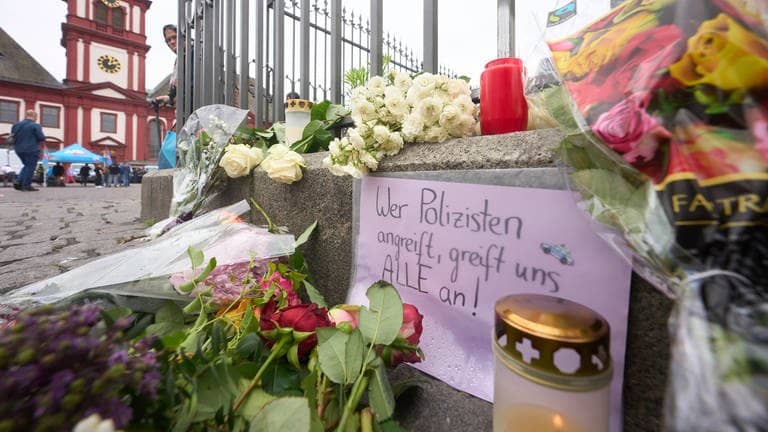 Nach der Messerattacke mit mehreren Verletzten in Mannheim erinnern Kerzen und Blumen an die Opfer. Auf dem Schild steht: „Wer Polizisten angreift, greift uns alle an“