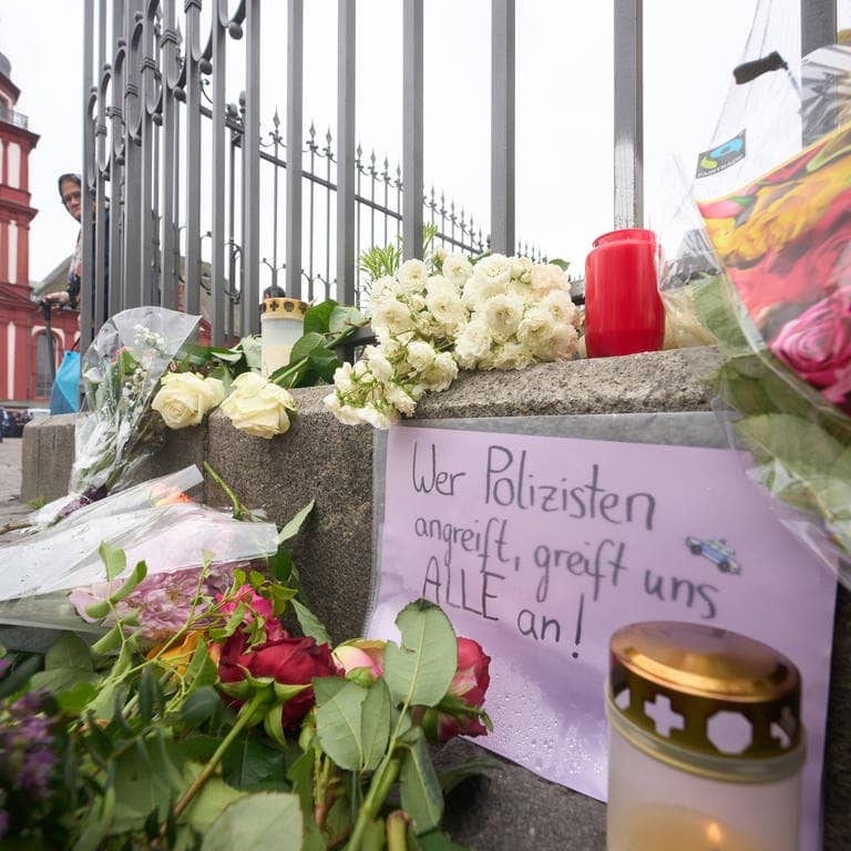 Nach der Messerattacke mit mehreren Verletzten in Mannheim erinnern Kerzen und Blumen an die Opfer. Auf dem Schild steht: „Wer Polizisten angreift, greift uns alle an“