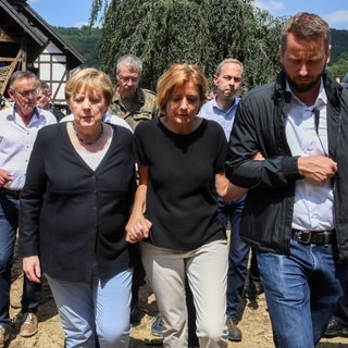 Juli 2021: Untergehakt bei der damaligen Bundeskanzlerin Angela Merkel läuft Dreyer durch das vom Hochwasser verwüstete Dorf Schuld bei Bad Neuenahr-Ahrweiler.
