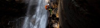 Symbolbild: Ein Canyoning-Sportler seilt sich neben einen Wasserfall ab. 