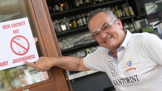 Der Inhaber des „Art Café“ in Pforzheim, Lambros Petrou, zeigt ein Schild mit der Aufschrift „Kein Eintritt mit Jogginghose“.
