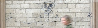 Eine Frau geht an einer Mauer mit beschädigten Kunstwerk Skelett von Künstler Harald Naegeli vorbei.