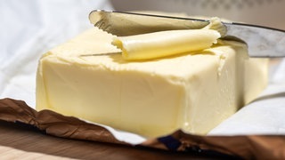 Ein Stück Butter liegt auf einem Tisch. Ein Messer schält ein Stück Butter ab. (Foto: dpa Bildfunk, picture alliance/dpa | Hendrik Schmidt) Ein Stück Butter liegt auf einem Tisch. Ein Messer schält ein Stück Butter ab.