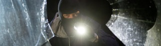 Ein fiktiver Einbrecher blickt an einem Haus durch eine eingeschlagene Fensterscheibe – Einbrecher in Wales hängt Wäsche auf, putzt, trinkt Wein