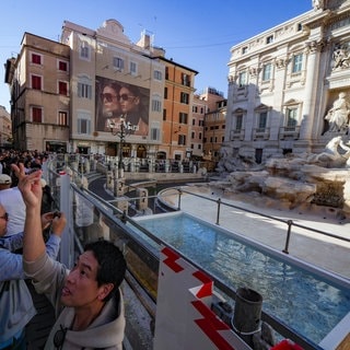 Touristen werfen Münzen in ein Becken vor dem Trevi-Brunnen in Rom.