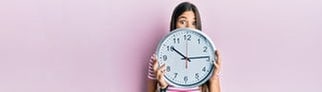 Eine Frau hält eine Uhr vor ihr Gesicht, weil sie weiß, dass im März die Uhren umgestellt werden und weitere Neuerungen auf sie warten