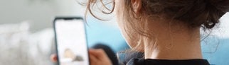 Eine Frau liegt auf einem Sofa und schaut sich ein Video auf der Social-Media-Plattform Instagram auf ihrem Handy an. – Auf Instagram & TikTok gibt es einen Trend: „Cortisol Detox“ & „Cortisol Face“. Ärzte warnen davor.