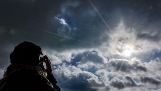 Symbolbild für partielle Sonnenfinsternis am 29. März: Eine Frau schaut mit Schutzbrille in die Sonne.