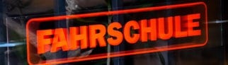 Ein Schild weist auf eine Fahrschule hin. Dort werden auch die Prüfungen für den Führerschein abgenommen.