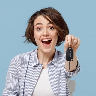 Symbolbild theoretische Führerscheinprüfung mit neuen Fragen vom 1. April 2025: Frau hält lachend einen Autoschlüssel in der Hand