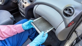 Jemand zieht einen Pollenfilter aus dem Auto. Einmal jährlich sollte man den wechseln.