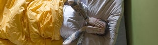 Ein Mann liegt im Bett und reibt sich die Augen. (Symbolbild für SWR3 Dialektüre)