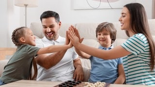Weniger Gewalt in der Erziehung von Kindern am Beispiel von Vater und Mutter mit ihren zwei Kindern, wie sie die Hände zusammenhalten