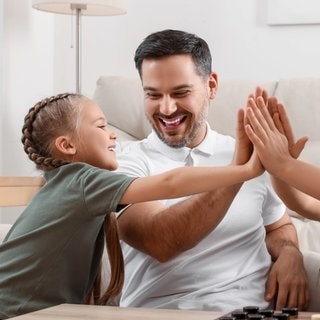 Weniger Gewalt in der Erziehung von Kindern am Beispiel von Vater und Mutter mit ihren zwei Kindern, wie sie die Hände zusammenhalten