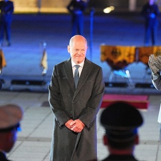 Der scheidende Bundeskanzler Olaf Scholz (M, SPD) lächelt, während Verteidigungsminister Boris Pistorius (l, SPD) und General Carsten Breuer, Generalinspekteur der Bundeswehr, applaudieren, beim großen Zapfenstreich der Bundeswehr anlässlich seiner Verabschiedung.
