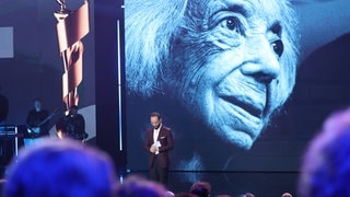 Pianist Igor Levit steht auf der Bühne des Deutschen Filmpreises und hält eine Trauerrede für die gestorbene Margot Friedländer, von der Foto im Hintergrund auf einer Leinwand zu sehen ist.