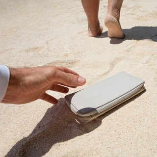 Ein verlorenere Geldbeutel am Strand. Eine Frau läuft weg, ein Mann greift danach. (Symbolbild)