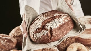 Jemand hält ein Brot in einem Tuch: Das belebteste Essen der Deutschen: Brot! Mehr zu Trends, Genuss und Zubereitung von einem Bäcker