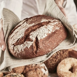 Jemand hält ein Brot in einem Tuch: Das belebteste Essen der Deutschen: Brot! Mehr zu Trends, Genuss und Zubereitung von einem Bäcker
