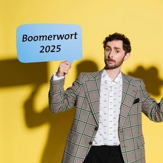 Ein Mann hält zwei Sprechblasen in die Luft mit der Aufschrift „Boomerwort 2025“ und Vorschlägen.