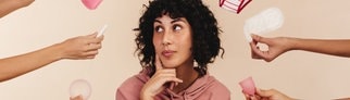 Eine Frau schaut nachdenklich zur Seite, viele Hände halten ihr Produkte für die Periode hin. Menstruation ist noch immer ein Tabuthema.