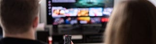 Symbolbild: Klage gegen Netflix wegen Preiserhöhung. Man sieht auf dem Bild ein Paar, einen Nann und eine Frau von hinten, die Fernsehen schauen.
