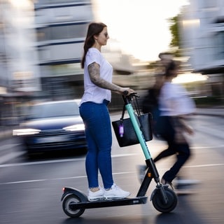 Frau auf dem E-Scooter fährt auf der Straße: Wie fährt man sicher und schützt sich vor Unfällen?