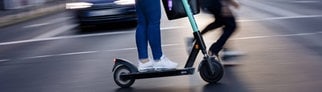 Frau auf dem E-Scooter fährt auf der Straße: Wie fährt man sicher und schützt sich vor Unfällen?