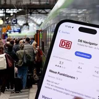 Symbolbild DB Navigator App und Menschen an einem Bahnhof.