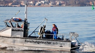 Florian Huber (rechts) und Philipp Schubert (Mitte) fahren auf einem Boot auf der Ostsee. Im Auftrag des Umweltministeriums Schleswig-Holstein und der Umweltstiftung WWF haben die beiden im März 2022 ein so genanntes Geisternetz vor Kiel geborgen. Die Netze sind eine Gefahr für Fische und Meeresvögel. Auch für Robben und Schweinswale können sie zu Todesfallen werden, wenn sich die Tiere in ihnen verfangen. (Foto: dpa Bildfunk, picture alliance/dpa | Frank Molter) Florian Huber (rechts) und Philipp Schubert (Mitte) fahren auf einem Boot auf der Ostsee. Im Auftrag des Umweltministeriums Schleswig-Holstein und der Umweltstiftung WWF haben die beiden im März 2022 ein so genanntes Geisternetz vor Kiel geborgen. Die Netze sind eine Gefahr für Fische und Meeresvögel. Auch für Robben und Schweinswale können sie zu Todesfallen werden, wenn sich die Tiere in ihnen verfangen.