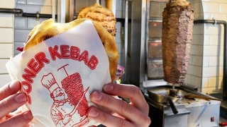 Döner-Logo auf einem Papier, in dem ein Döner eingepackt ist vor Döner-Spießen. Jetzt ist klar, wer das Bild erfunden hat.
