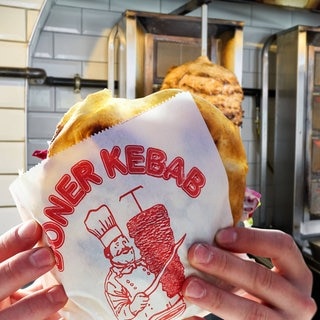 Döner-Logo auf einem Papier, in dem ein Döner eingepackt ist vor Döner-Spießen. Jetzt ist klar, wer das Bild erfunden hat.