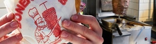 Döner-Logo auf einem Papier, in dem ein Döner eingepackt ist vor Döner-Spießen. Jetzt ist klar, wer das Bild erfunden hat.