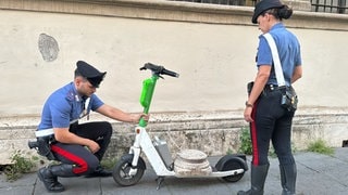 Zwei Carabinieri stehen fassungslos neben dem E-Scooter, auf dem die antike Marmorsockelplatte liegt. 