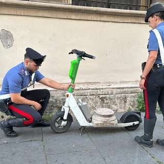 Zwei Carabinieri stehen fassungslos neben dem E-Scooter, auf dem die antike Marmorsockelplatte liegt. 