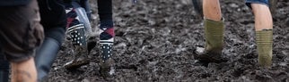Menschen mit Gummistiefeln laufen durch Schlamm, also fast schon klassisches Wetter bei Rock am Ring.