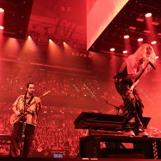 Linkin Park auf Deutschland Tour: Mike Shinoda spielt links auf dem Bild Gitarre und Sängerin Emily Armstrong singt bei einem Konzert in der Barclays Arena in Hamburg im September 2024.