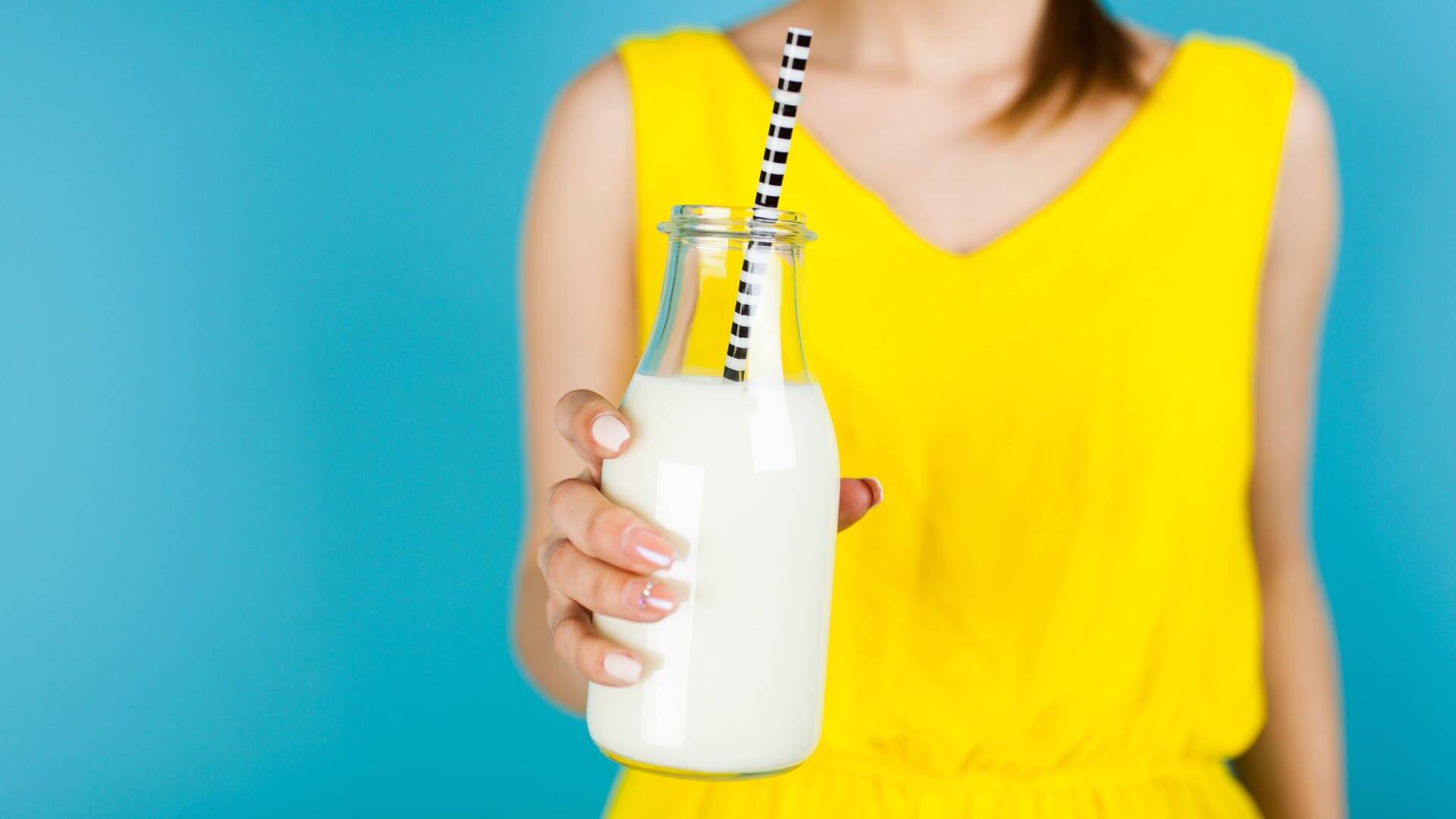 Junge Frau hält eine Milch-Glasflasche mit Strohhalm in der Hand (Foto: Adobe Stock/George Dolgikh)